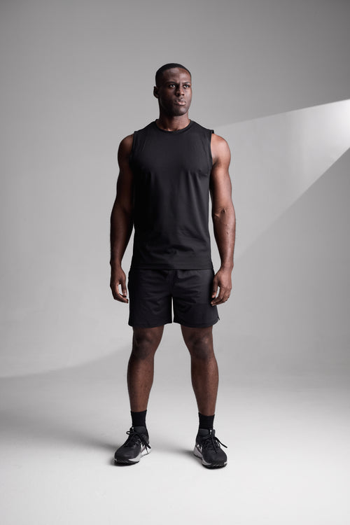 Man wearing a black sleeveless shirt and shorts standing against a gray background