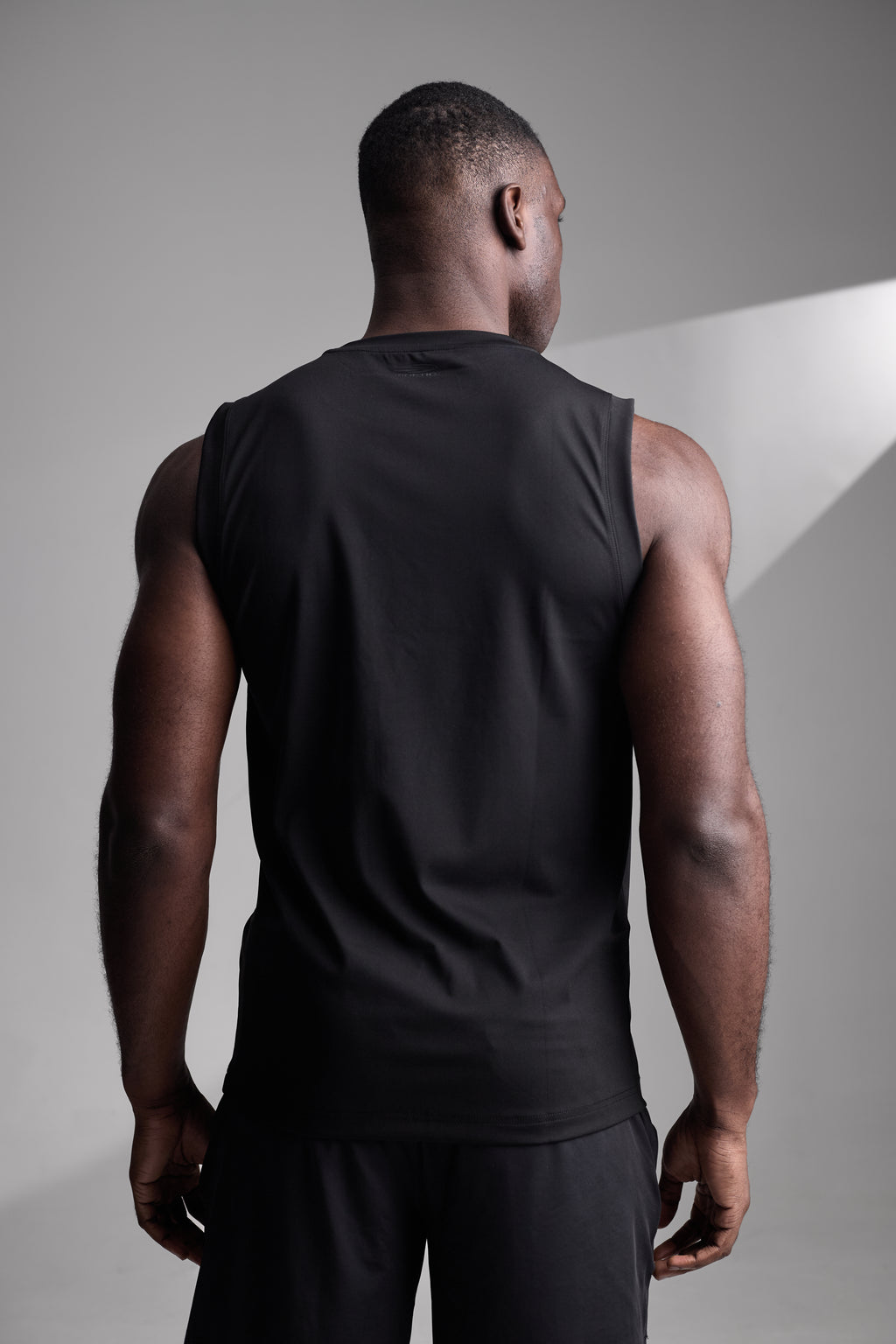 Man wearing a black sleeveless shirt against a gray background