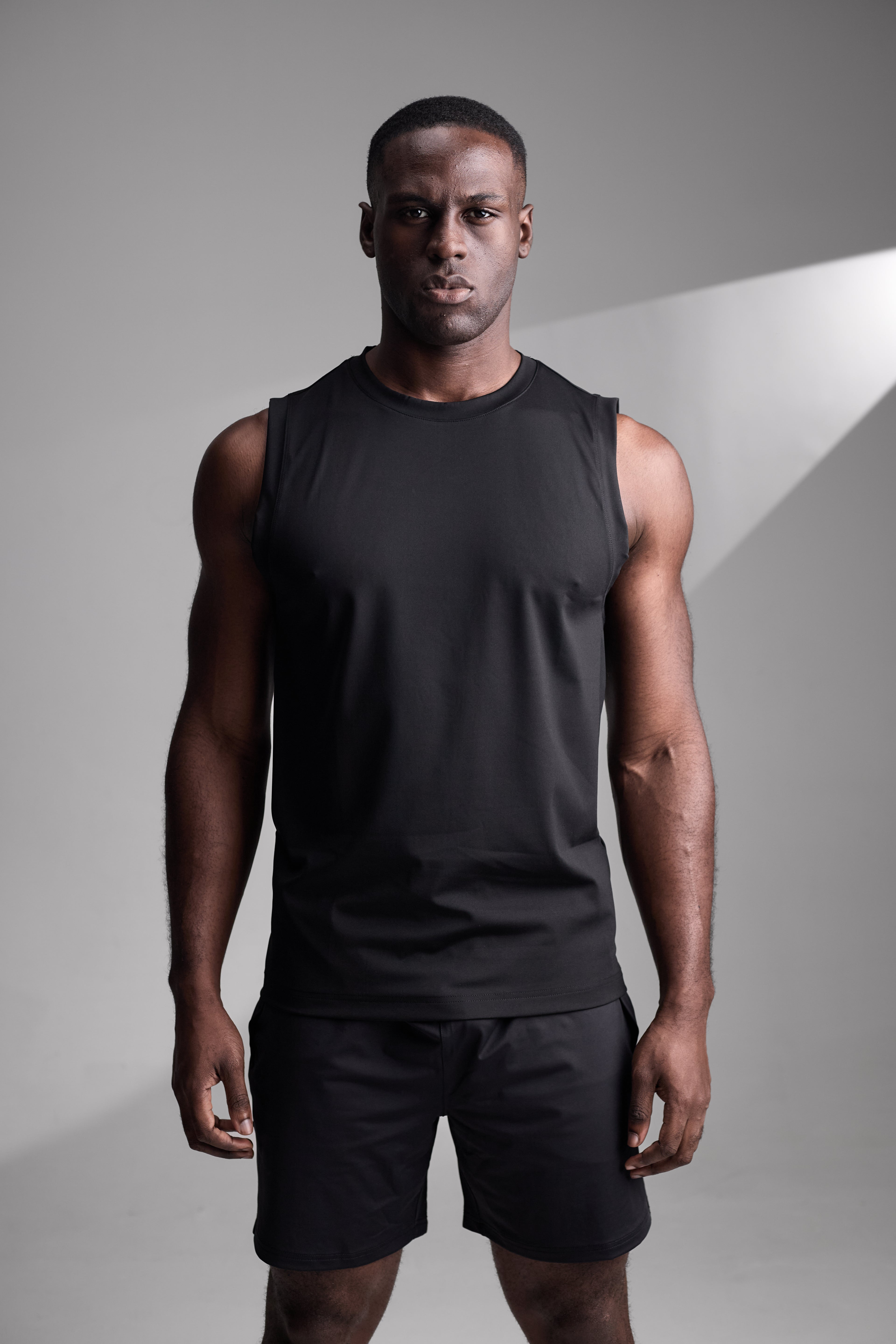 Man wearing a black sleeveless shirt and shorts on a gray background
