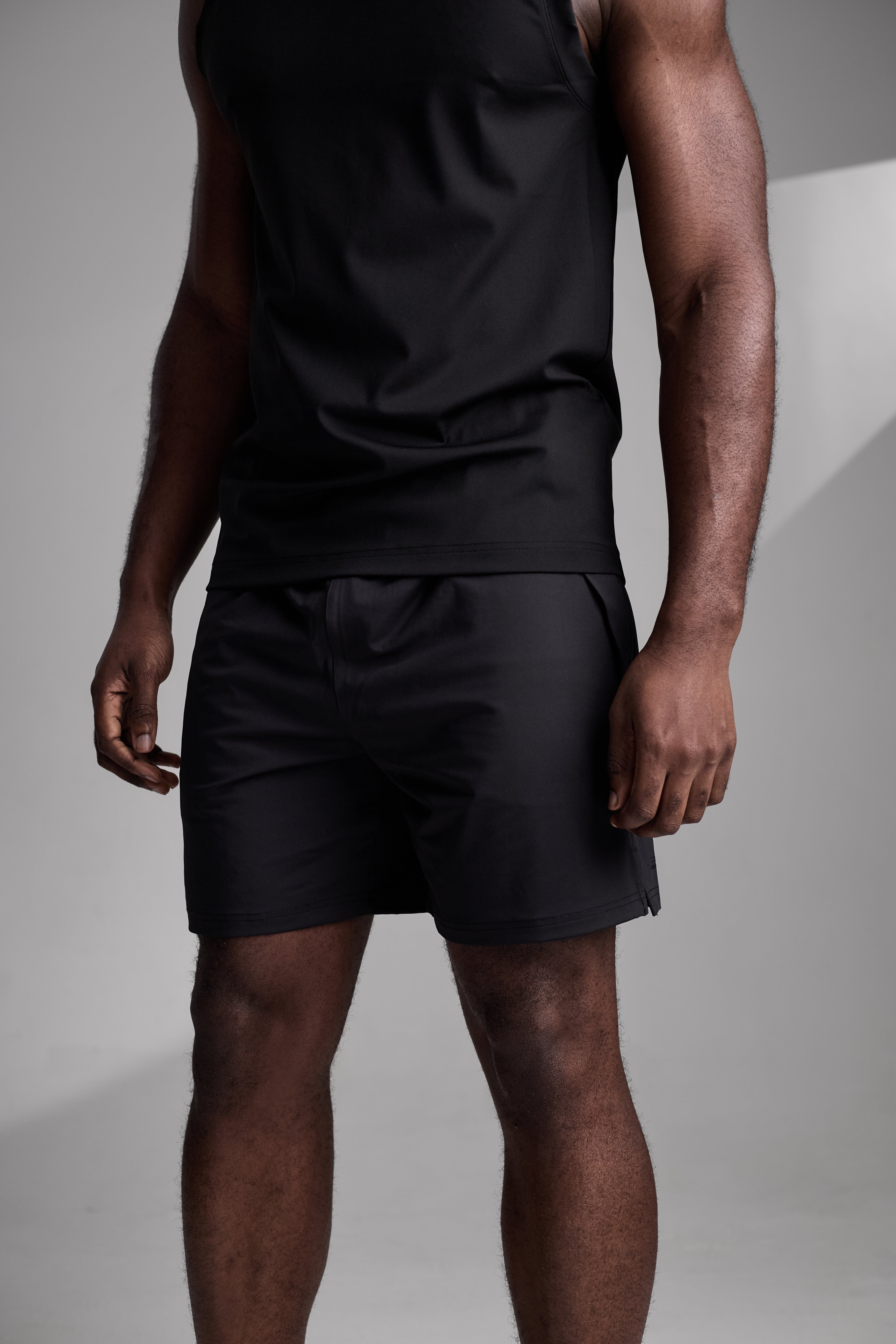 Person wearing a black fitness tank top and shorts on a plain background