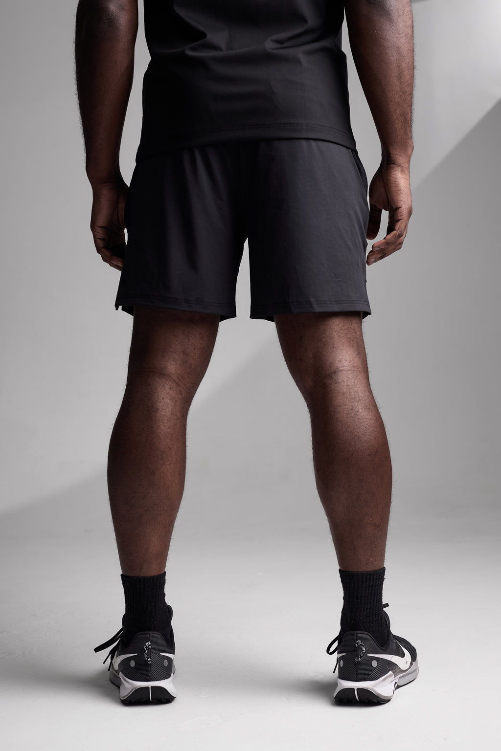 Person wearing black athletic shorts and shoes on a light gray background
