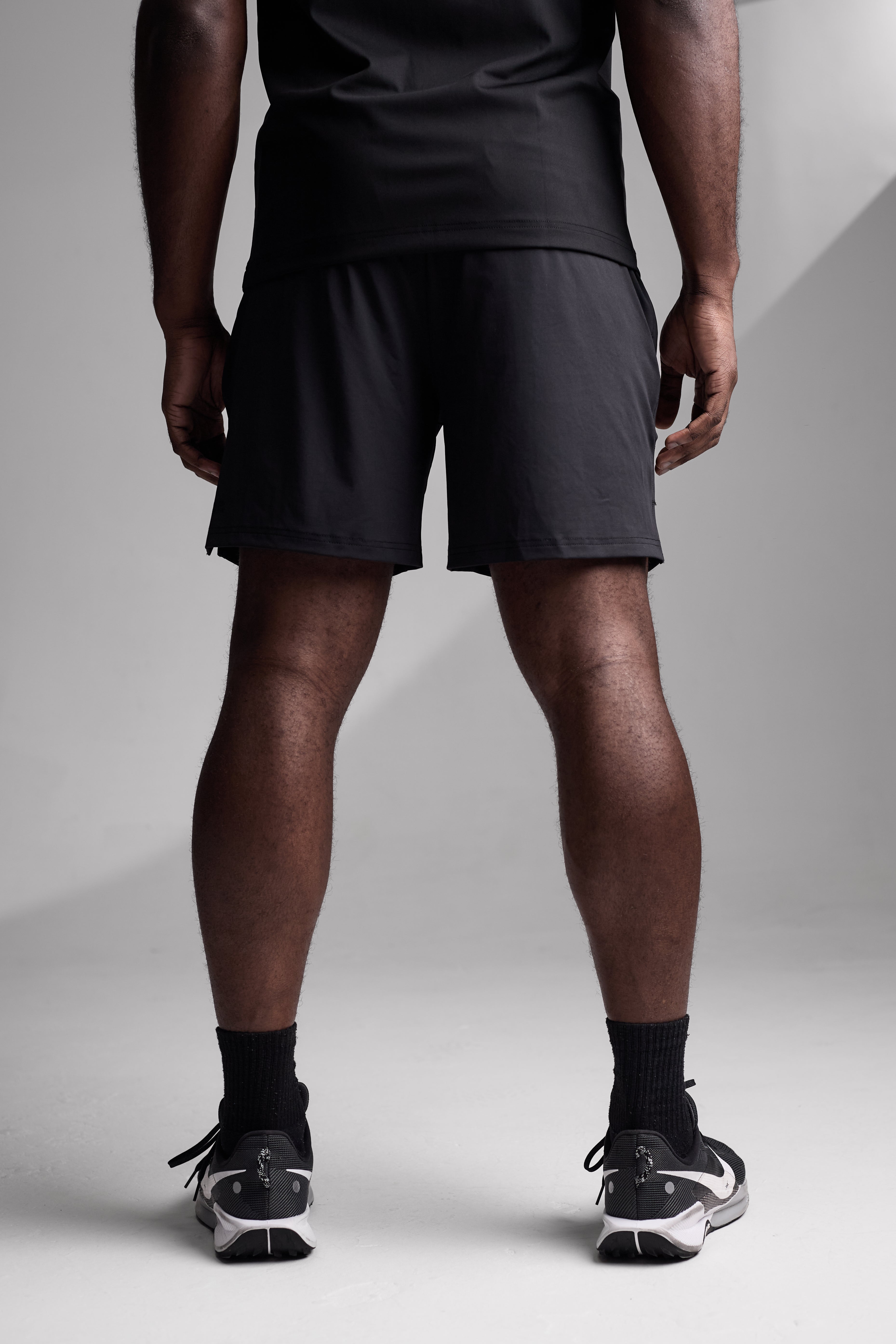 Person wearing black athletic shorts and shoes on a light gray background