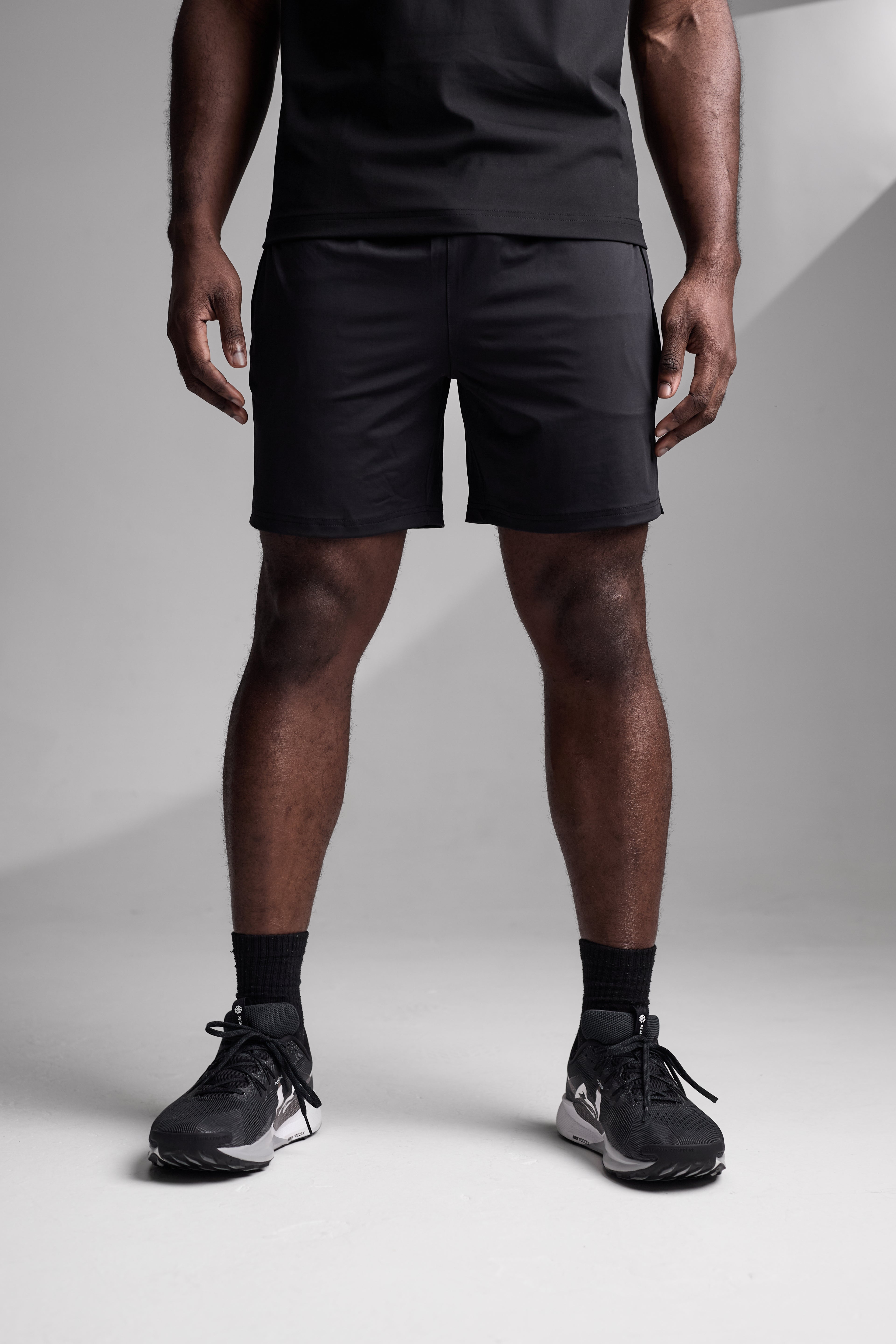 Person wearing black athletic shorts and shoes on a light gray background