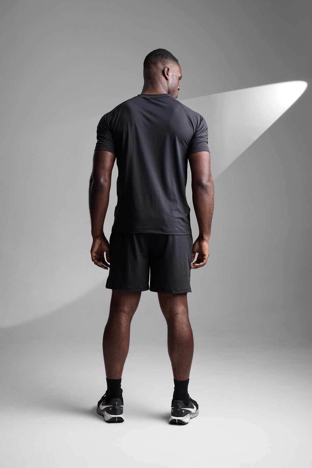 Man wearing a black athletic outfit standing against a gray background