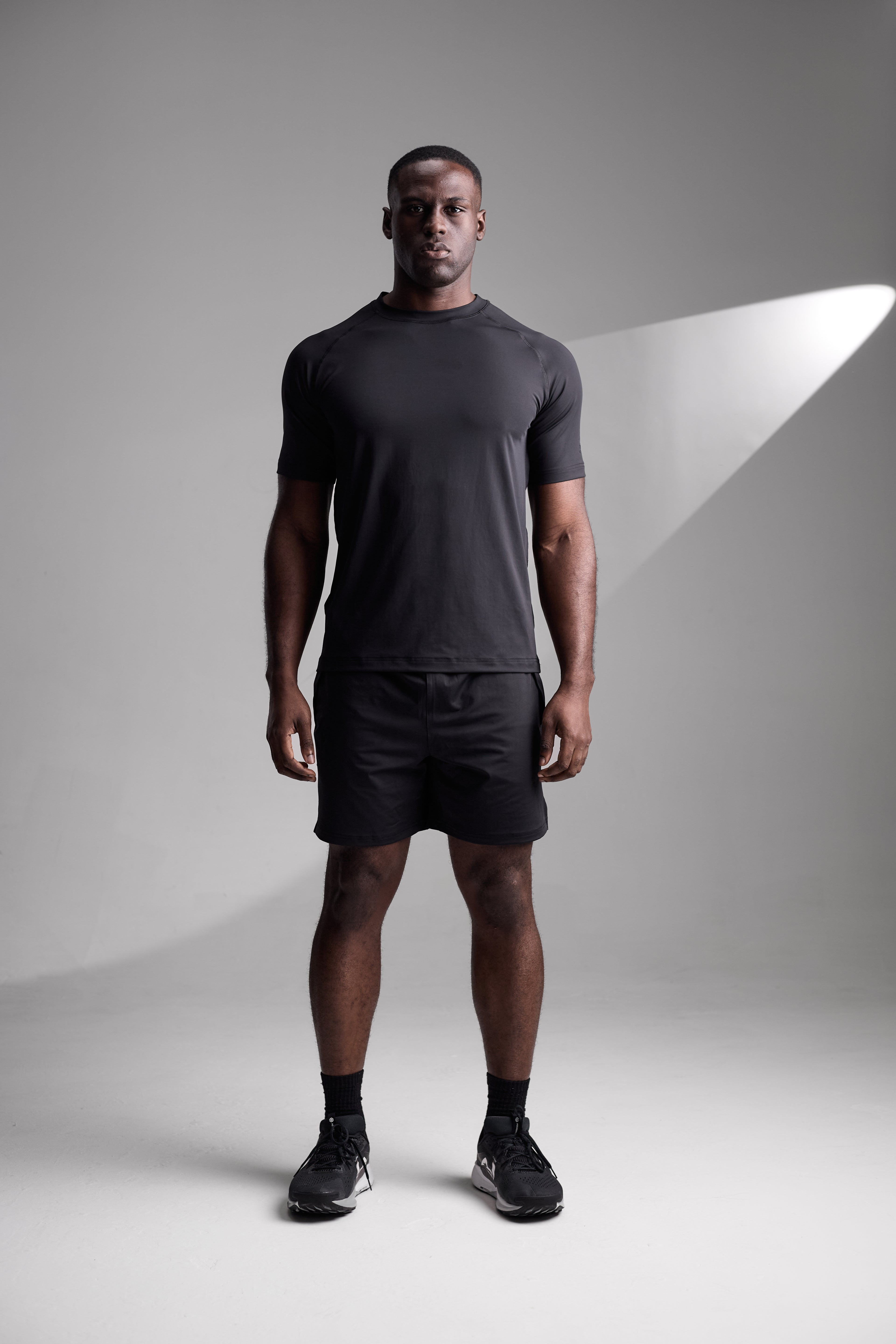Man wearing a black t-shirt and shorts standing against a gray background