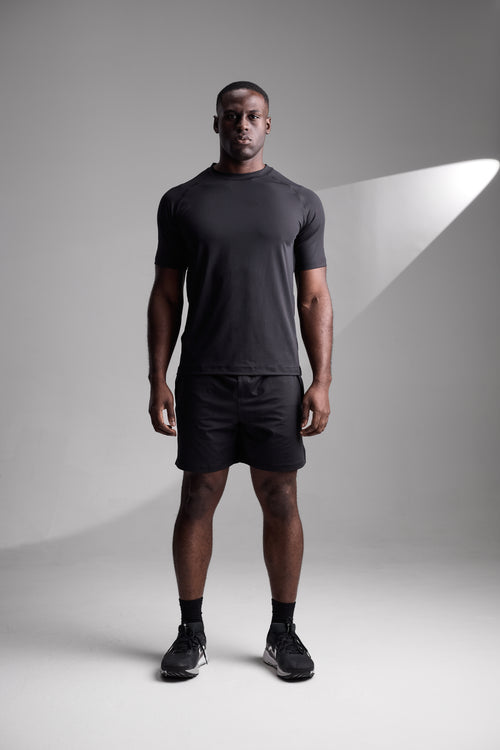 Man wearing a black t-shirt and shorts standing against a gray background