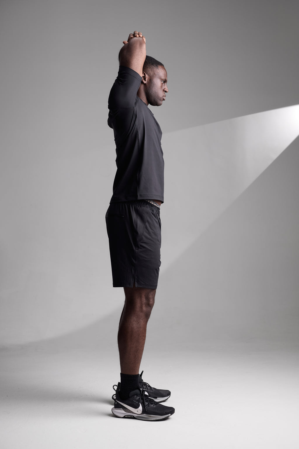 Man in athletic wear stretching against a plain background