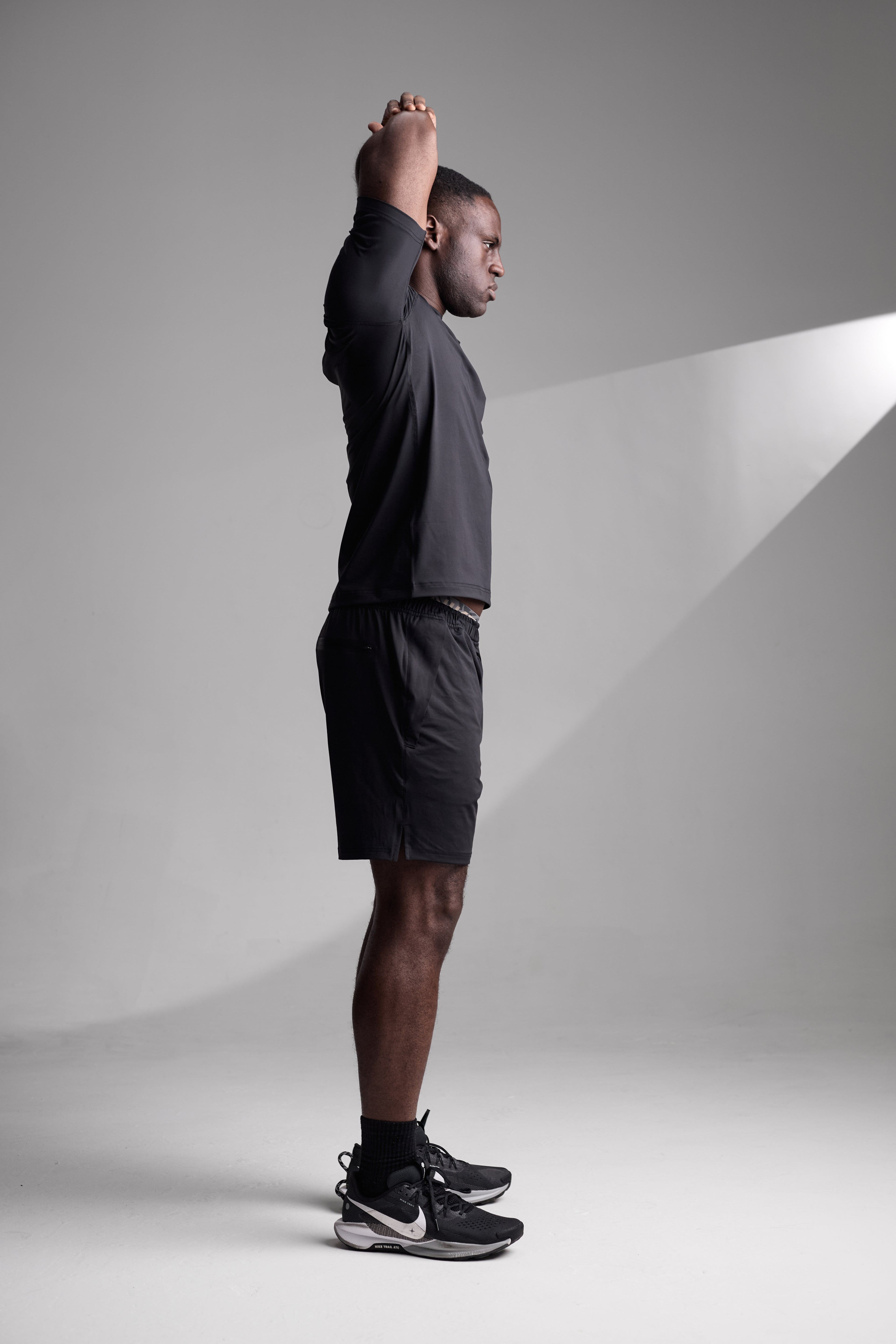 Man in athletic wear stretching against a plain background