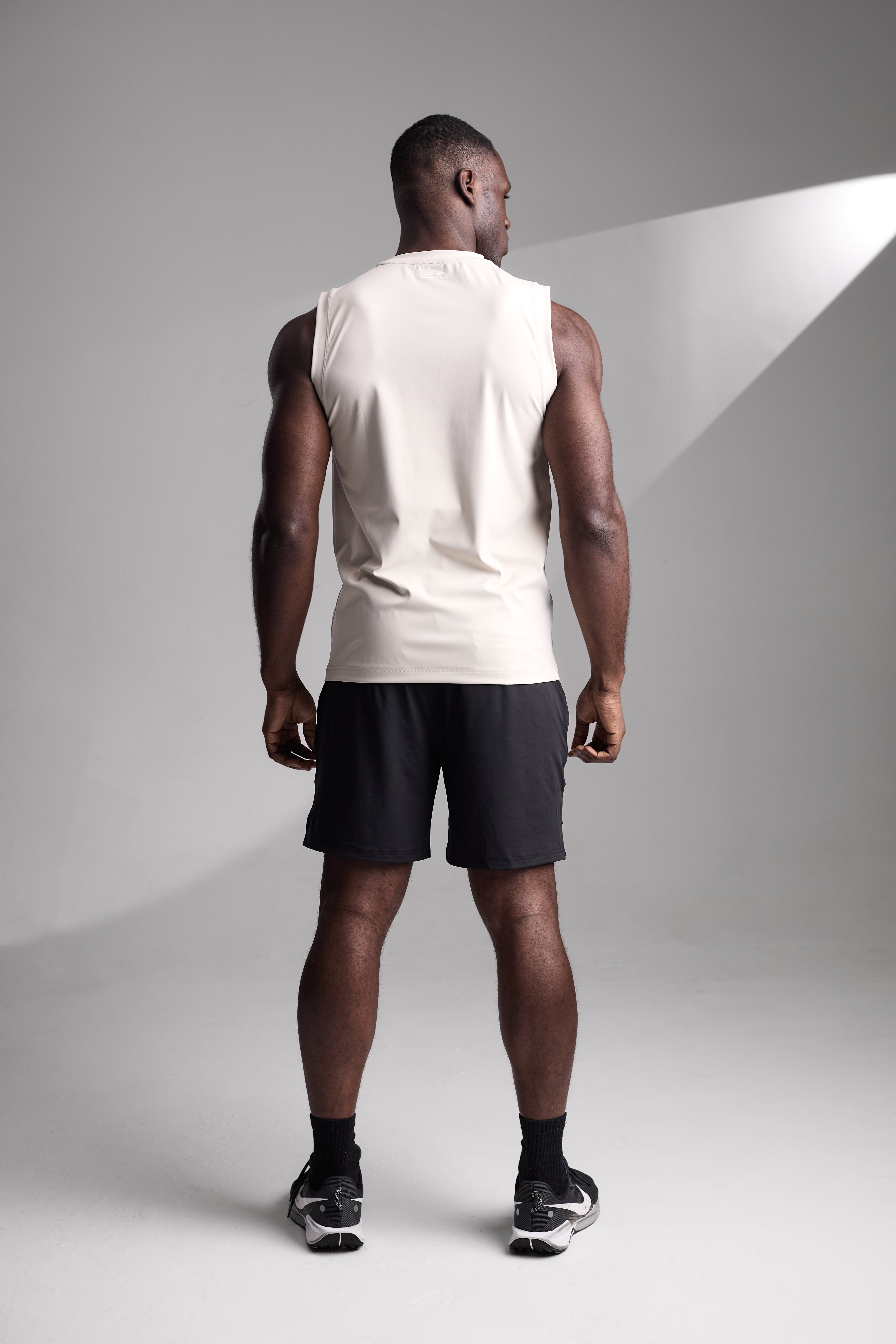 Man wearing an apricot sleeveless shirt and black shorts on a gray background