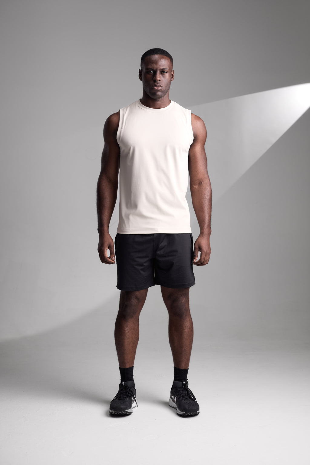 Man wearing a apricot fitness tank top and black shorts standing against a gray background
