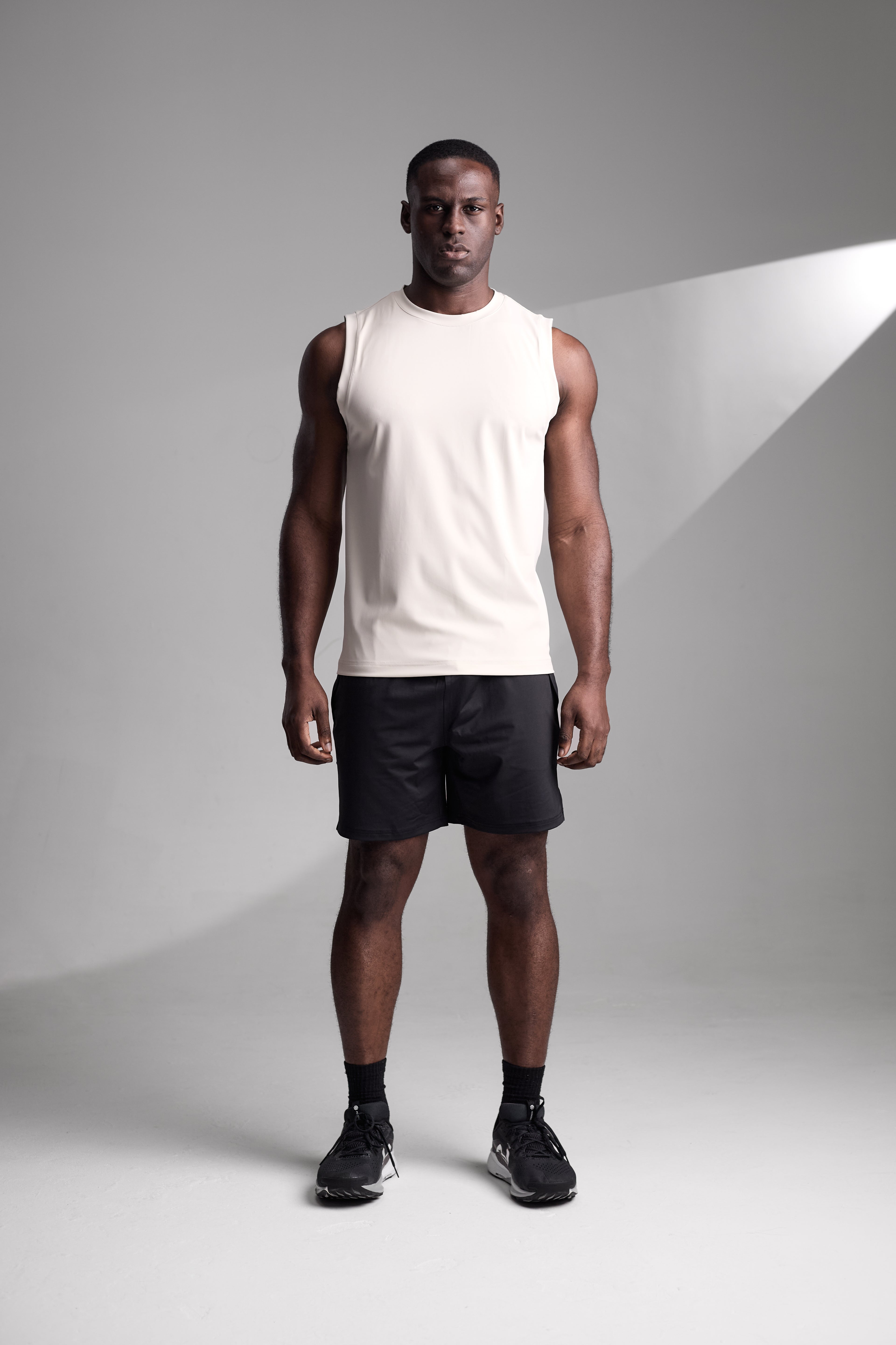 Man wearing a apricot fitness tank top and black shorts standing against a gray background
