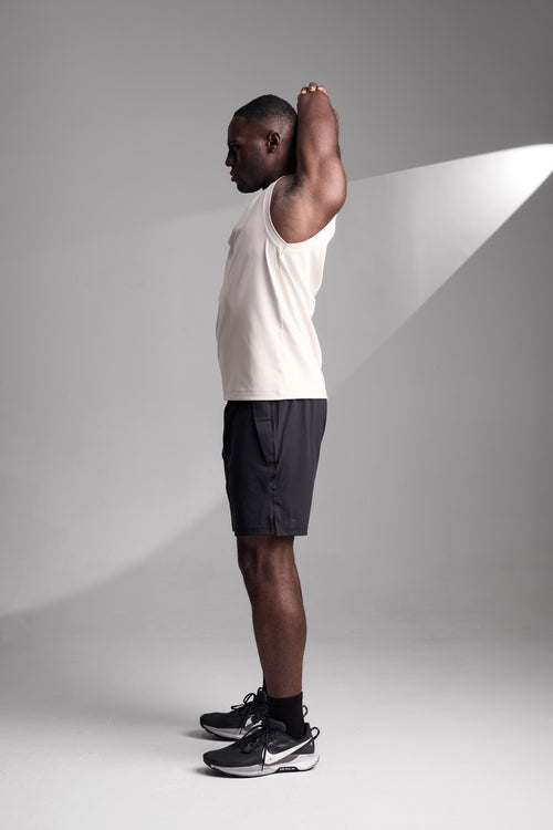 Man in a apricot tank top and black shorts standing against a gray background