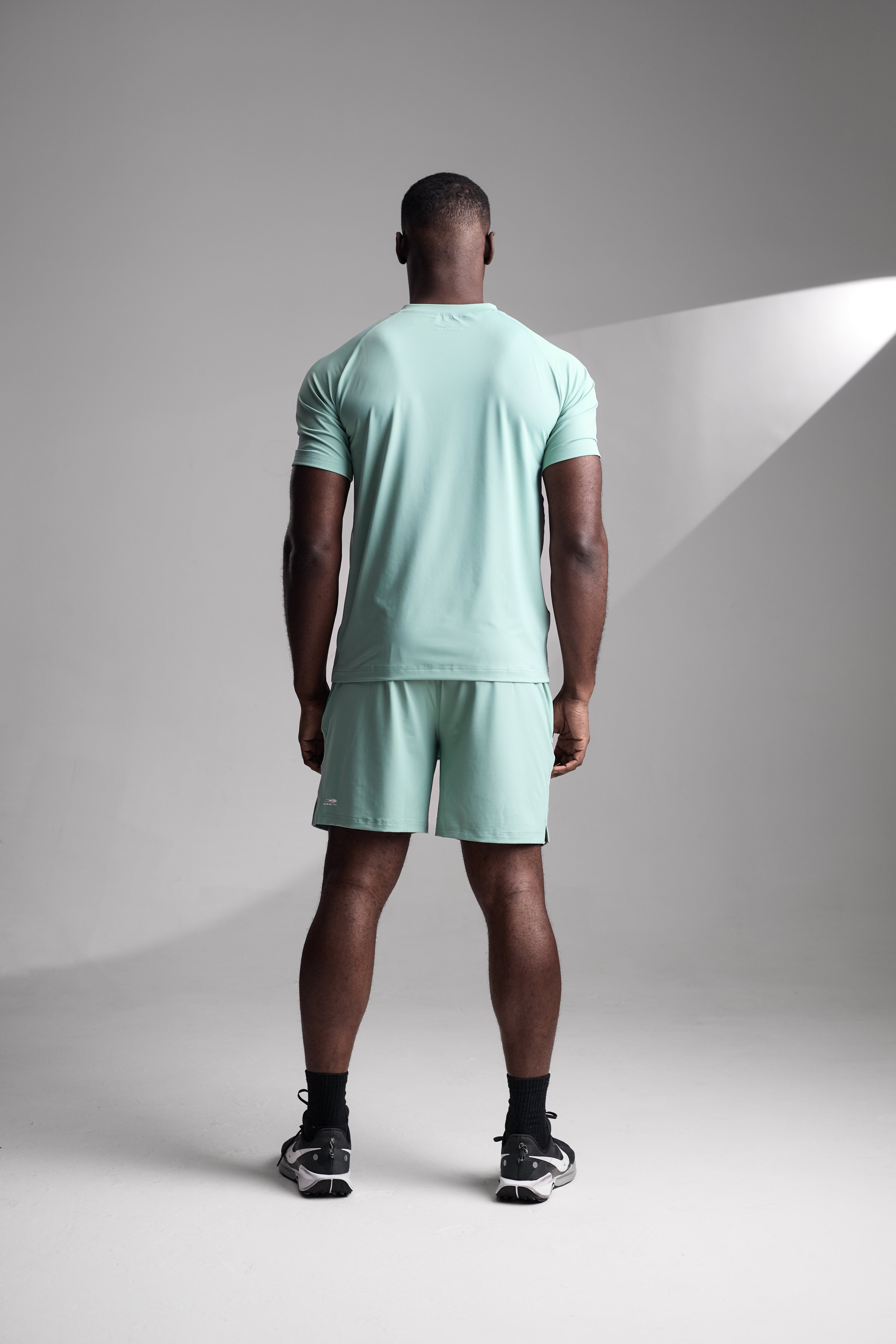 Man wearing a light green t-shirt and shorts standing against a gray background