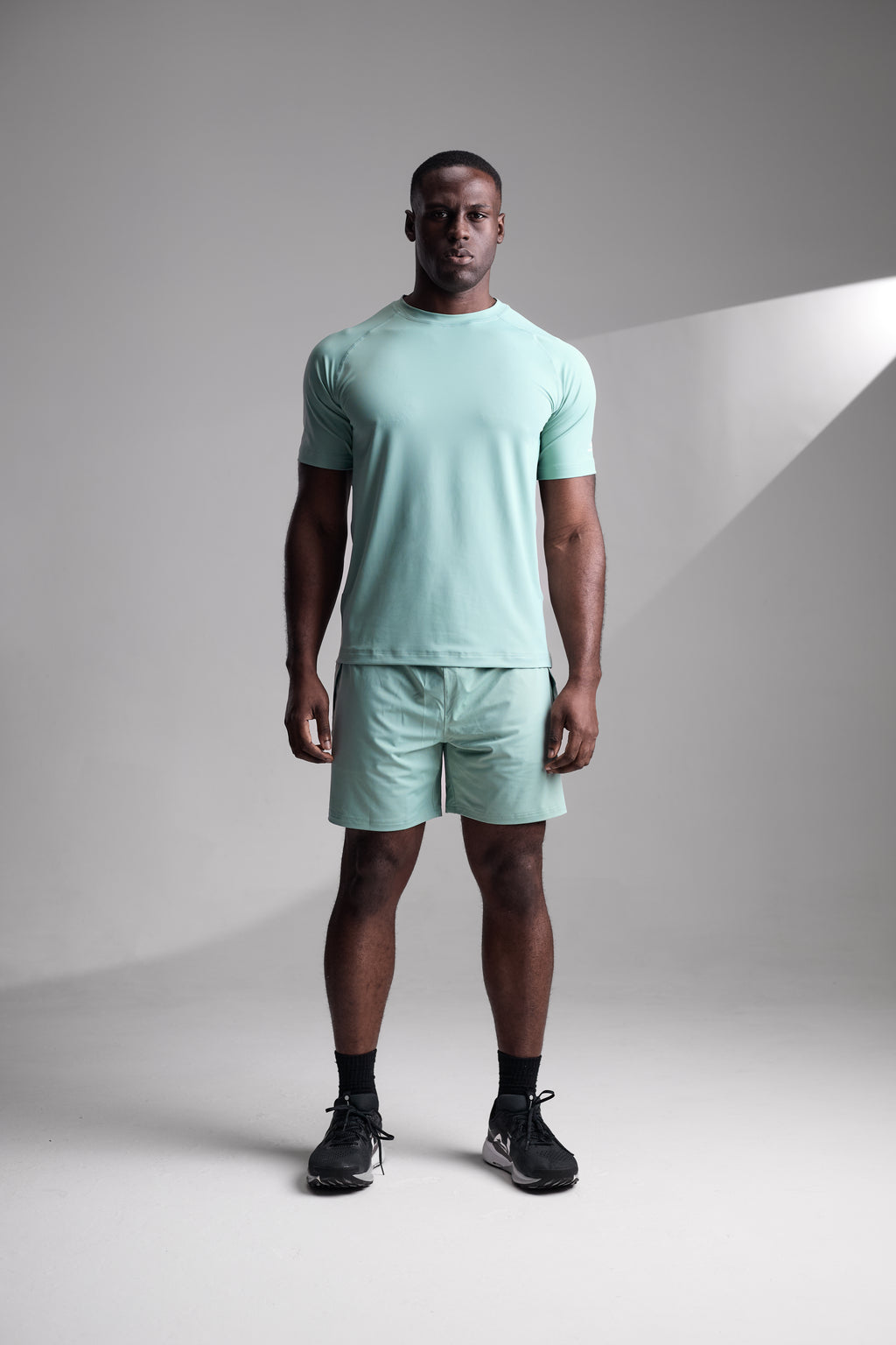 Man wearing a light green t-shirt and shorts set on a gray background