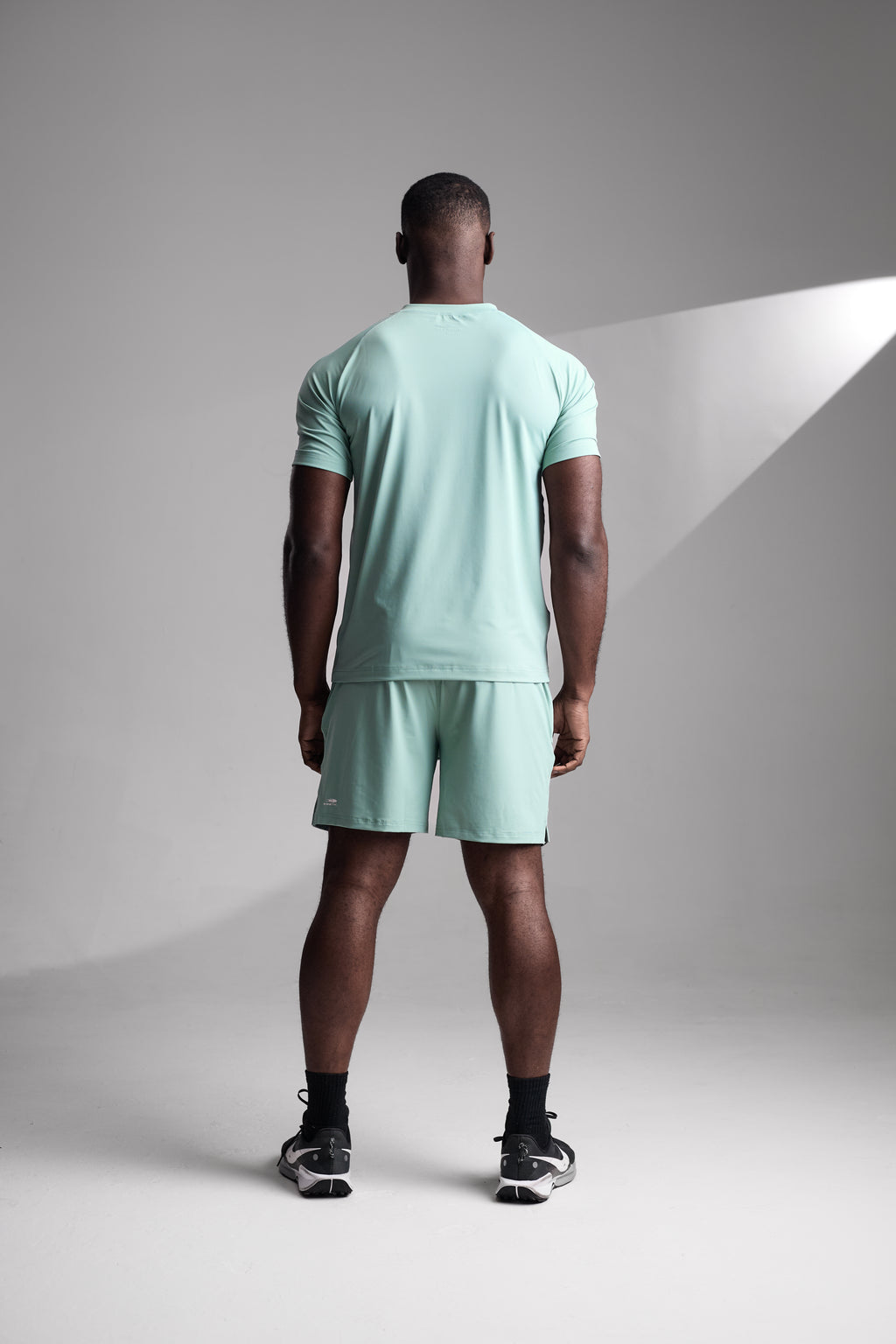 Man wearing a light green t-shirt and shorts standing against a gray background