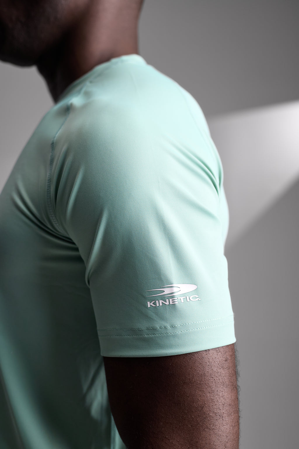 Person wearing a light green athletic shirt with 'kinetic' logo on a neutral background