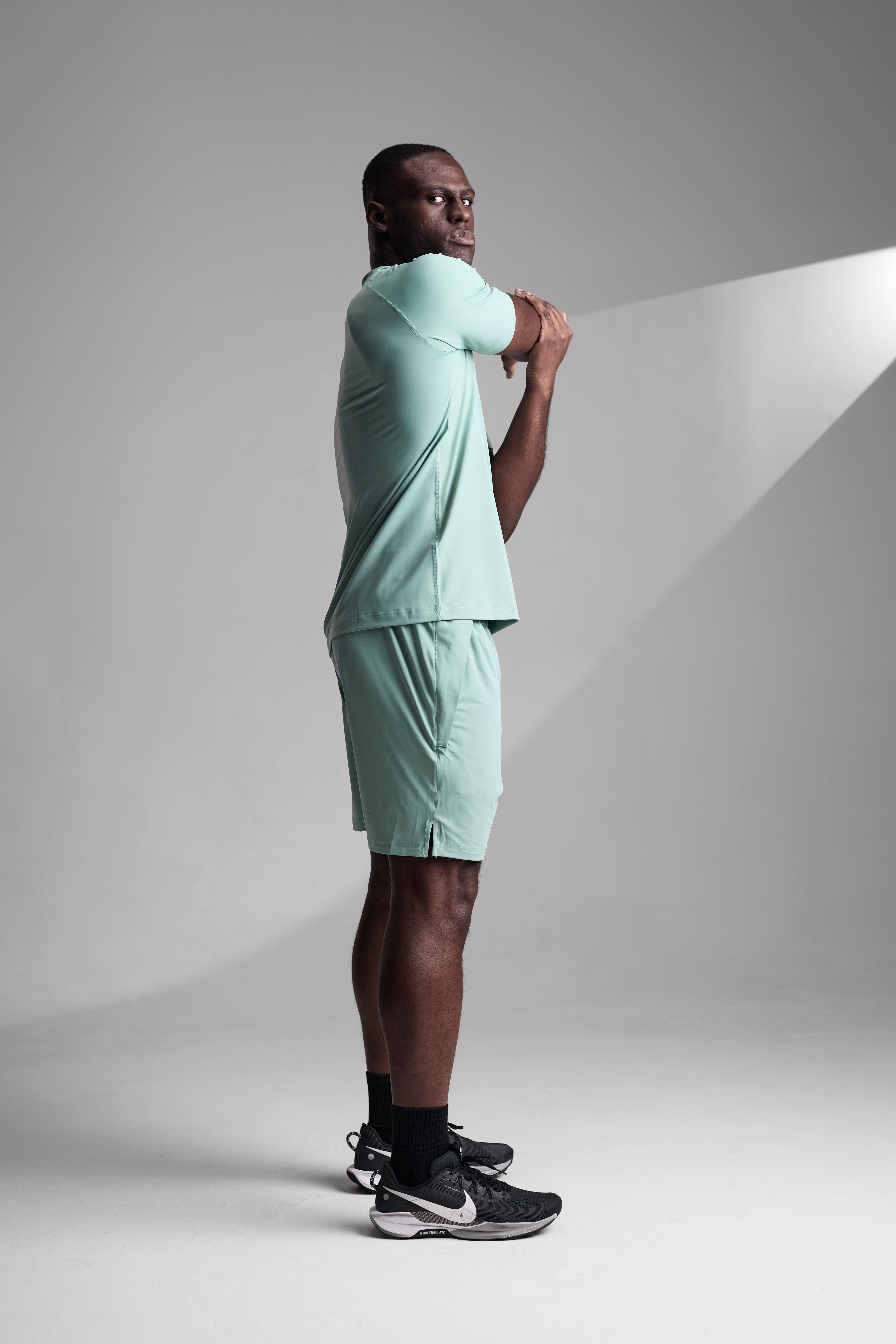 Man wearing a light green athletic outfit with black Nike shoes on a gray background