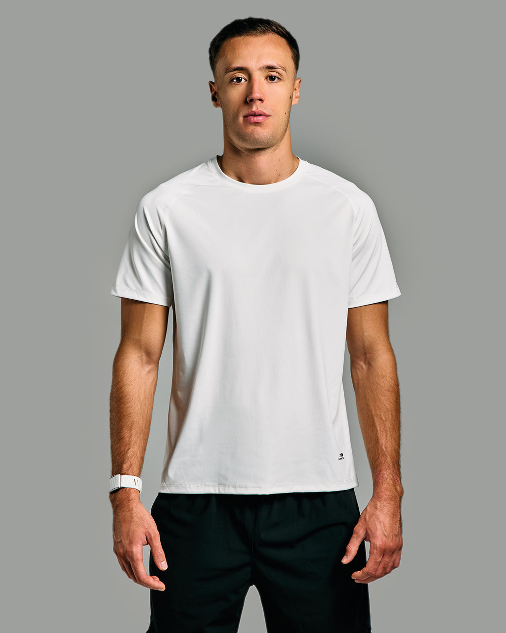 Man wearing a white t-shirt and black pants against a gray background