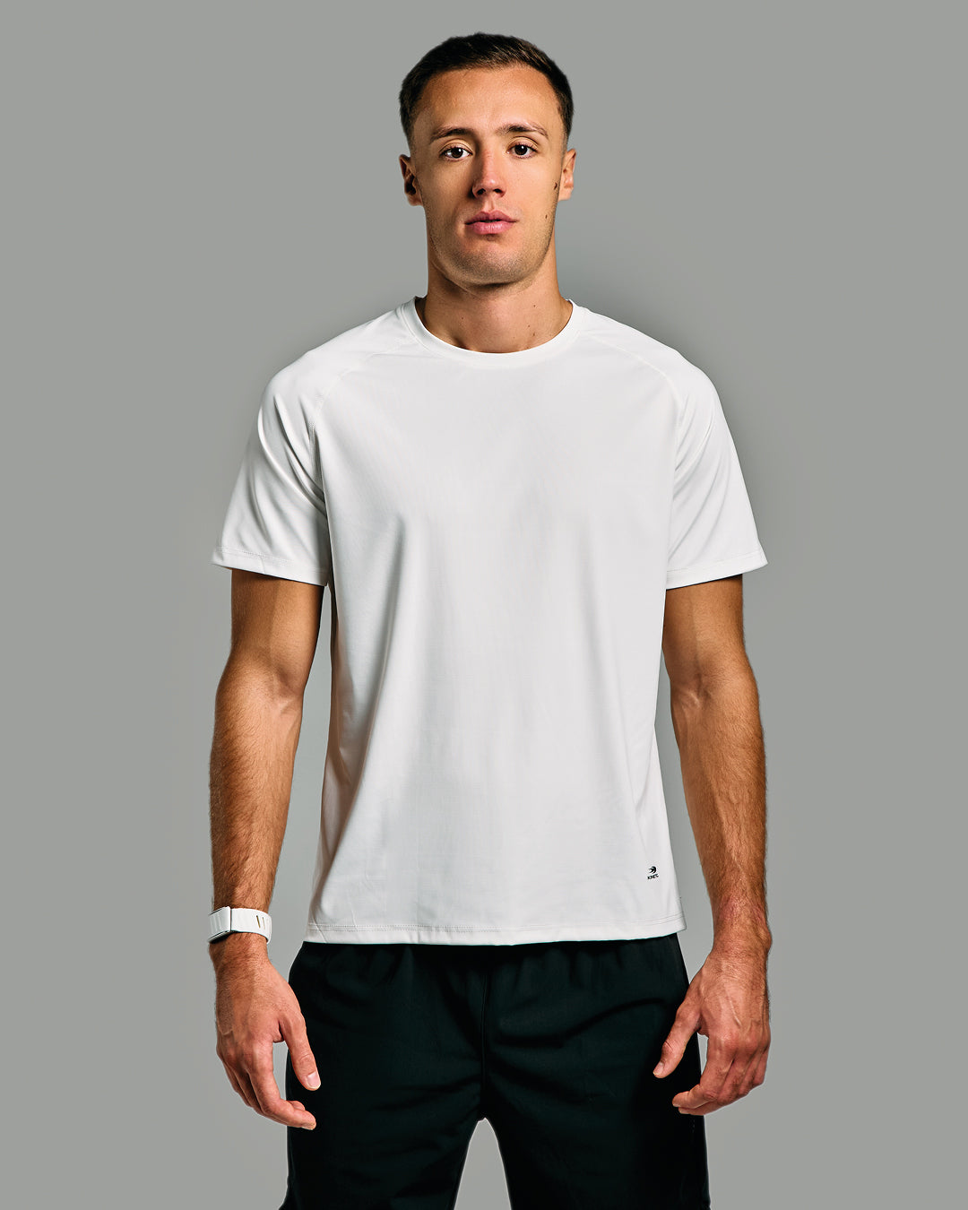 Man wearing a white t-shirt and black pants against a gray background