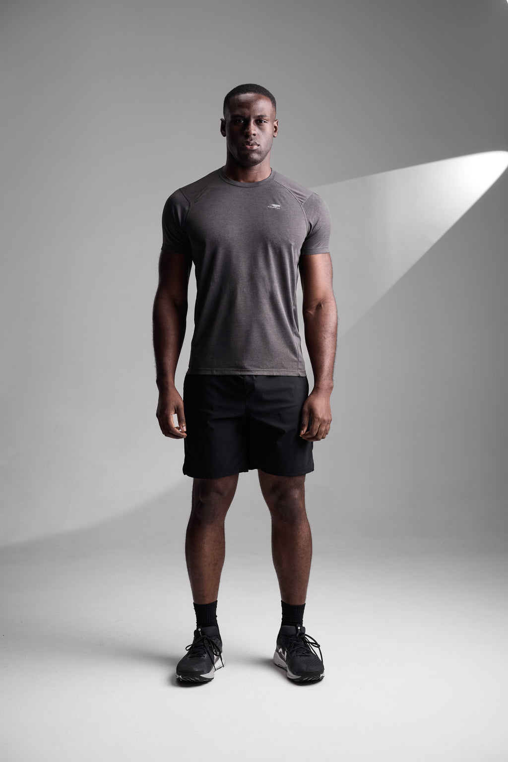Man wearing a gray athletic shirt and black shorts on a gray background