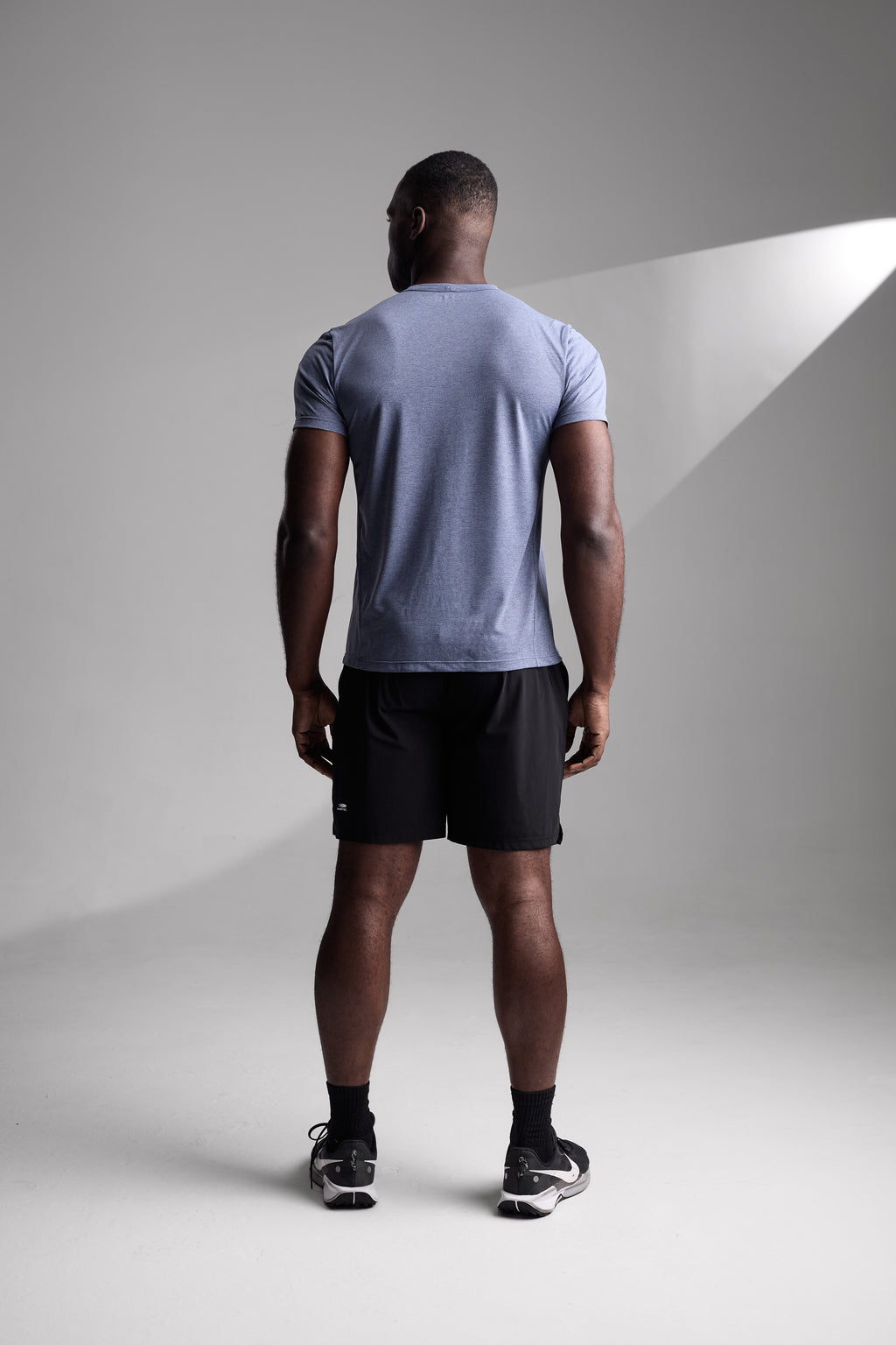 Person wearing a light blue fitness t-shirt and black shorts standing against a gray background