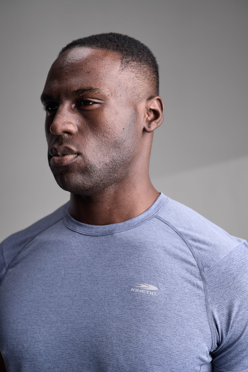 Man wearing a blue athletic fitness shirt with a brand logo on a gray background