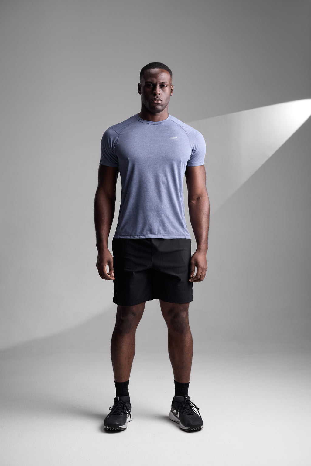 Man wearing a light blue t-shirt and black shorts standing against a gray background