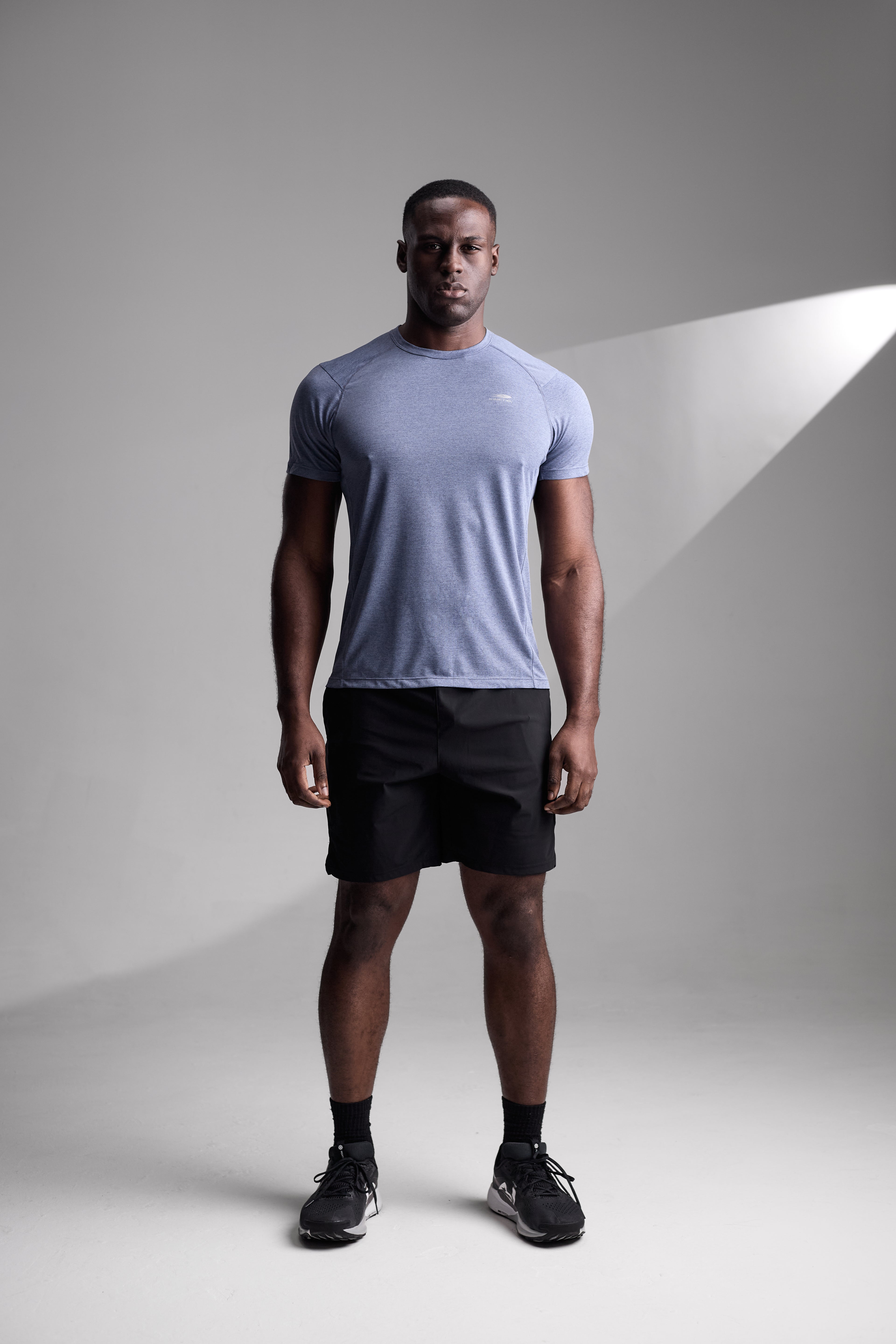 Man wearing a light blue t-shirt and black shorts standing against a gray background