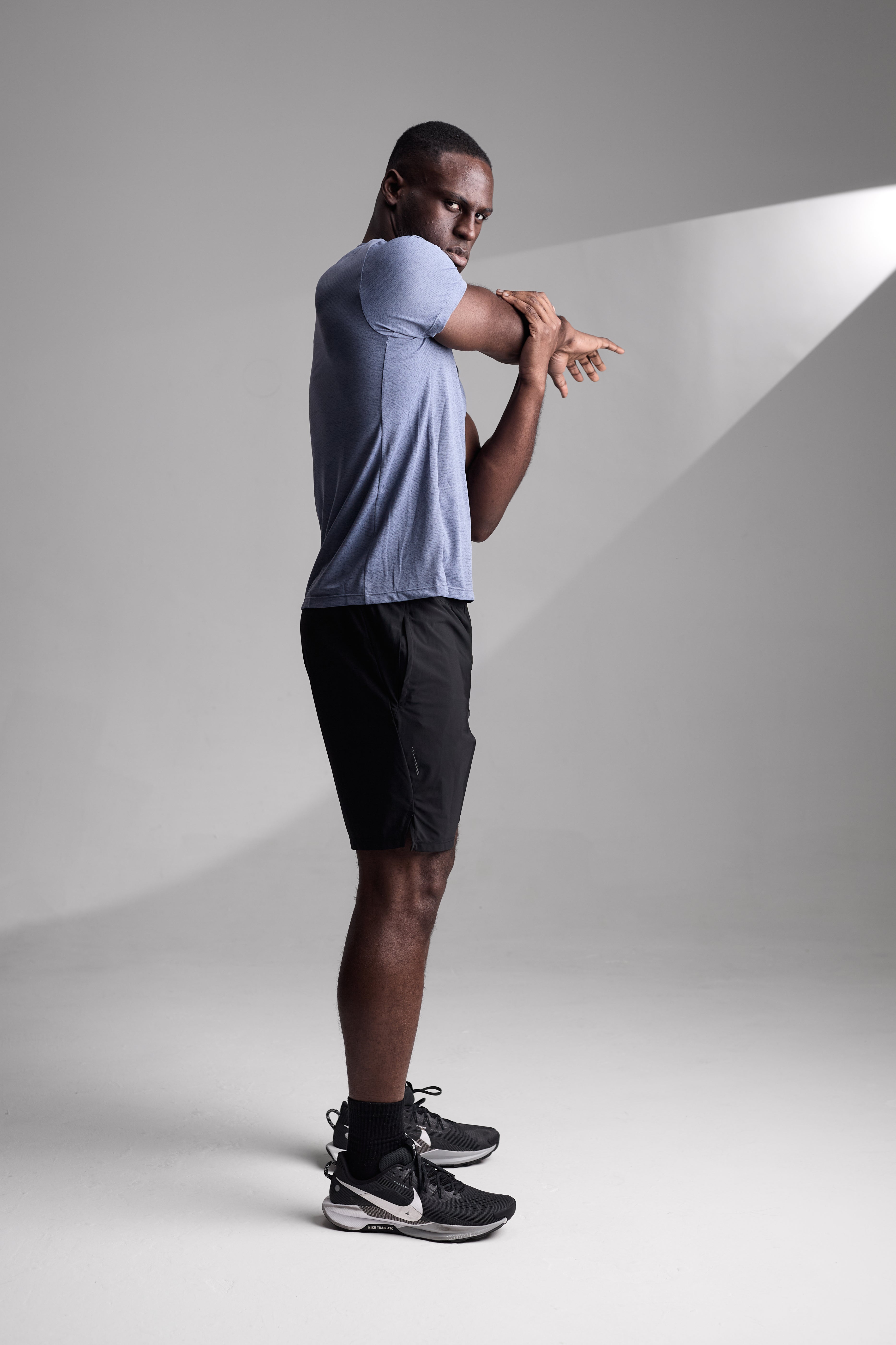 Athletic man stretching his arm in light blue fitness t-shirt on a plain background