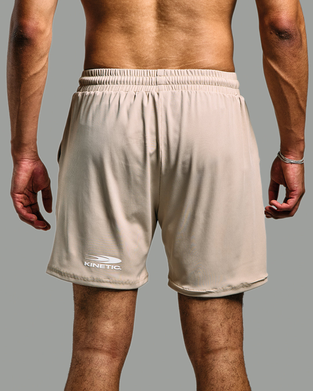 Nude athletic shorts with 'Kinetic' branding on a gray background