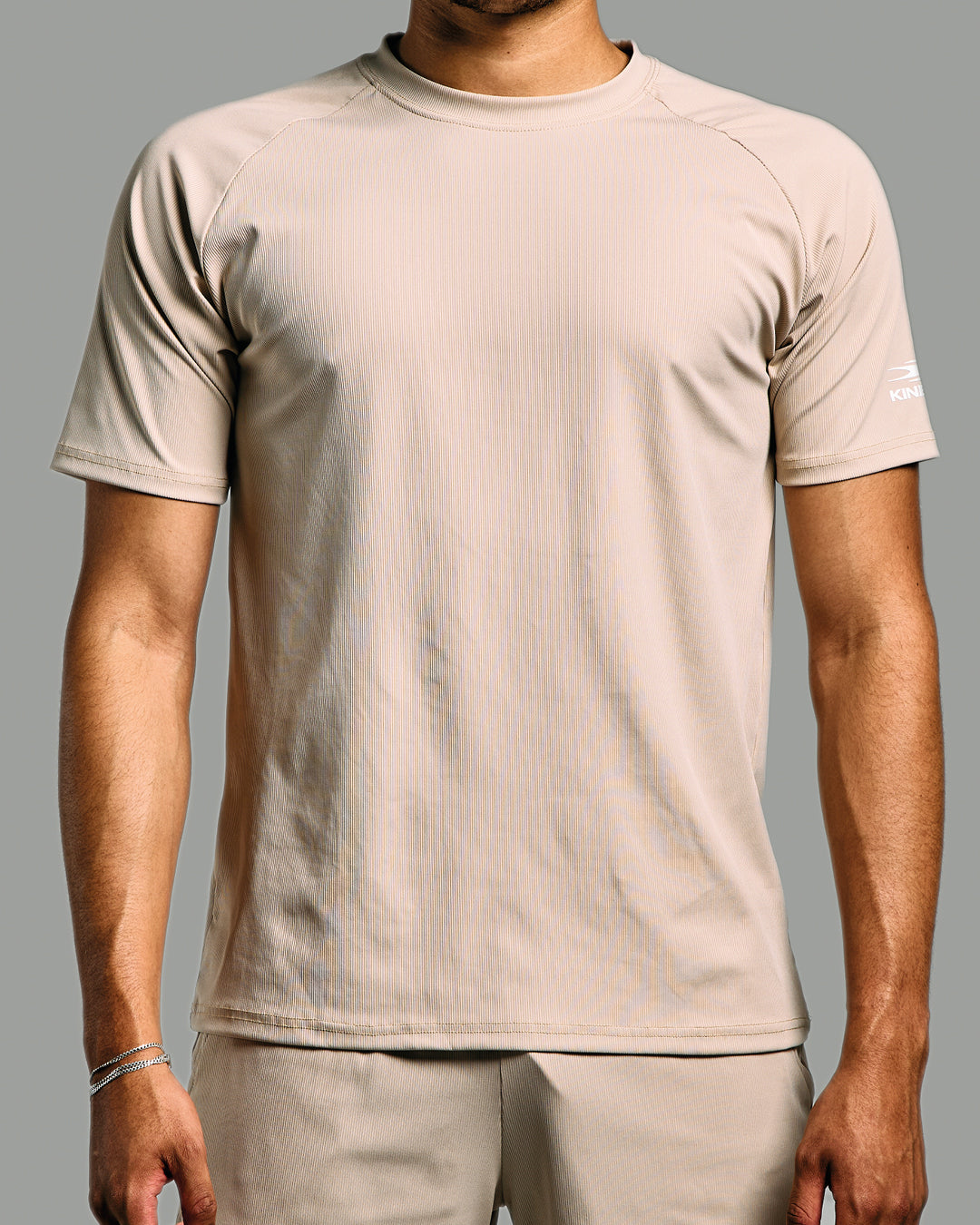 Person wearing a beige t-shirt and pants on a gray background
