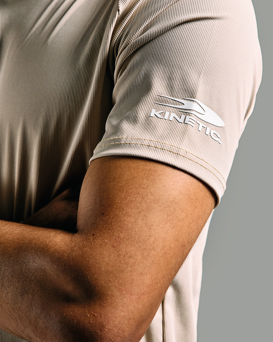 Close-up of a person wearing a beige shirt with 'Kinetic' logo on sleeve against a gray background