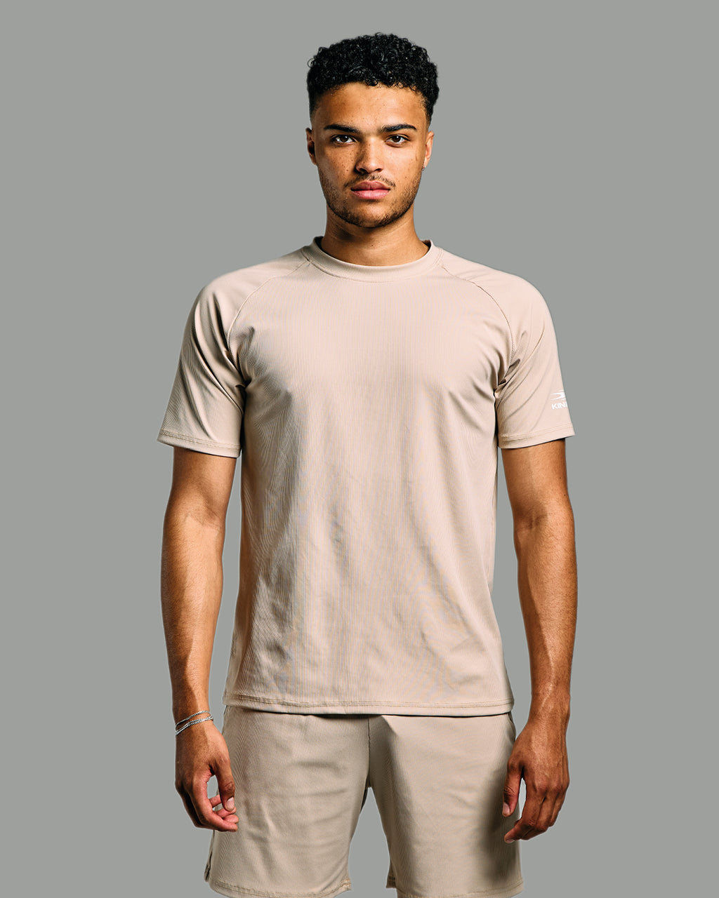 Man wearing a beige t-shirt and shorts on a gray background