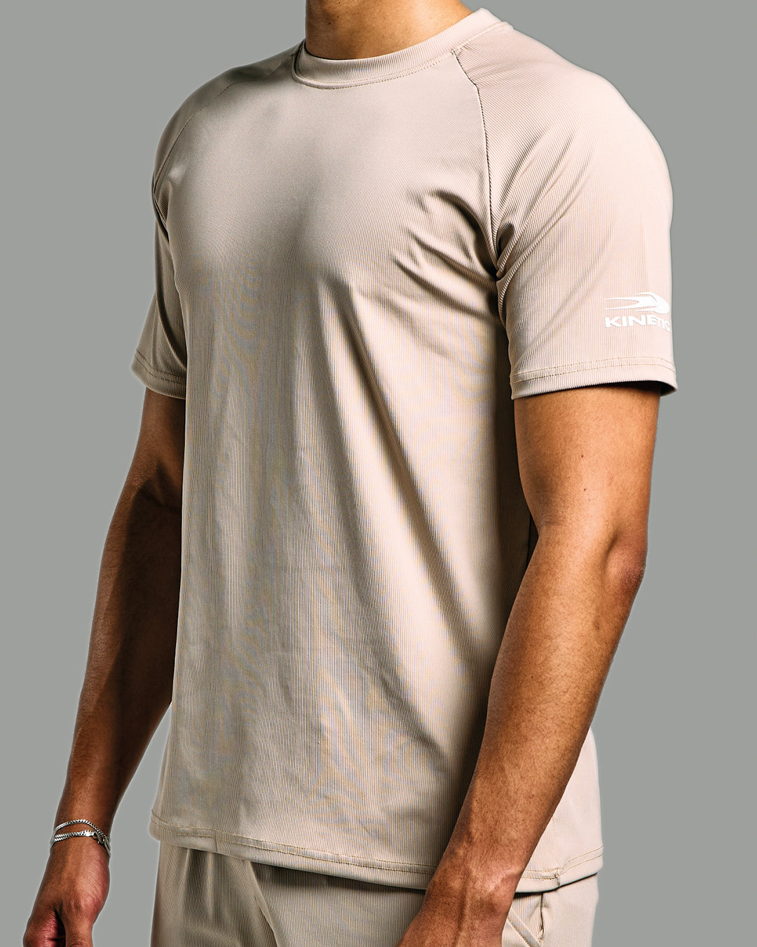 Person wearing a beige t-shirt with a brand logo on a gray background